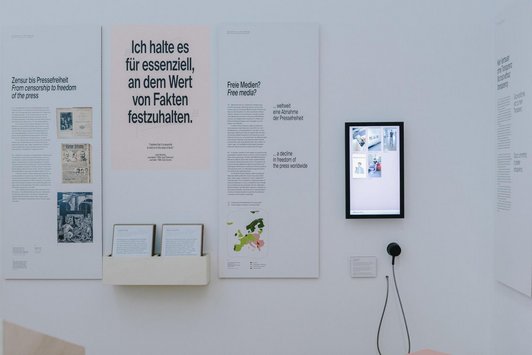 Wand mit Bildschirm, Kopfhöhrer und bedruckten Tafeln 