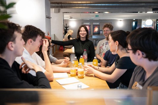 Jugendliche und zwei Erwachsene sitzen gut gelaunt um Tisch