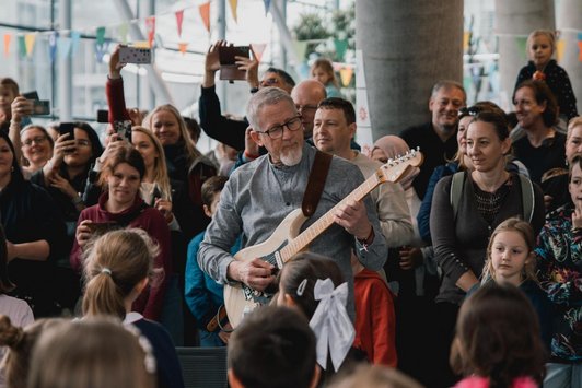 Mann spielt E-Gitarre umgeben von Kindern und Erwachsenen,