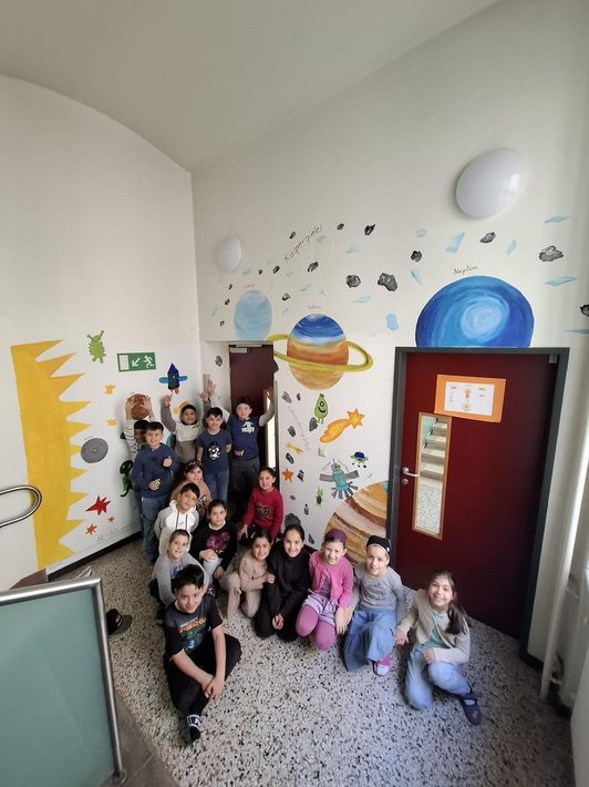 Schulklasse sitzt in Stiegenhaus vor Wandmalerei eines Weltalls