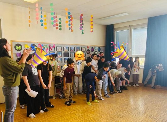 Schüler/innen verbeugen sich in Kassenzimmer, Lehrerin steht applaudierend daneben