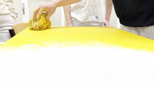 Nahaufnahme von Hand mit Schwamm beim Verteilen von gelber Farbe auf weißer Fläche