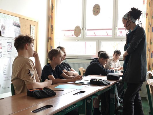 Foto eines Workshops mit sechs Schülern sitzen im Klassenraum, davor die Workshopleiterin.