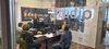 vier Schüler/innen sitzen in einem Radiostudio an einem Tisch und lesen in ein Mikro Texte, die vor Ihnen liegen.