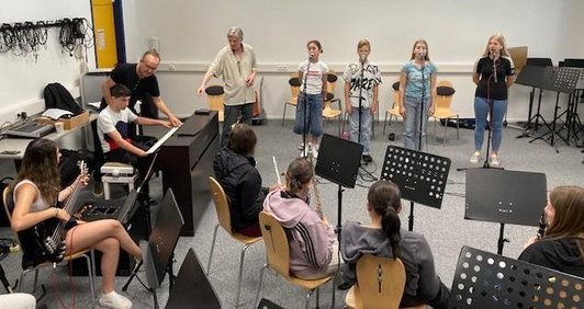 Schüler/innen und zwei Männer beim Singen und Musizieren