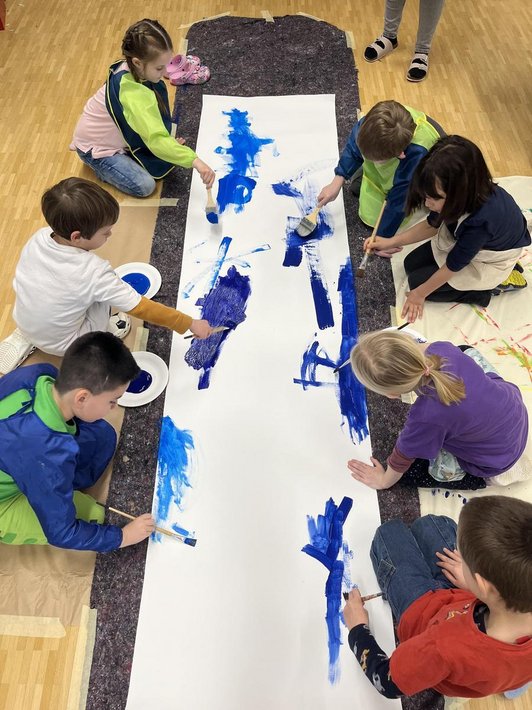 Kinder knien am Boten und bemalen lange weiße Leinwand mit blauer Farbe