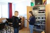 Foto von wwei Schülerinnen im Musiksaal, eine hält ein Triangel, eine hat Kopfhörer auf und ein Aufnahmegerät in der Hand