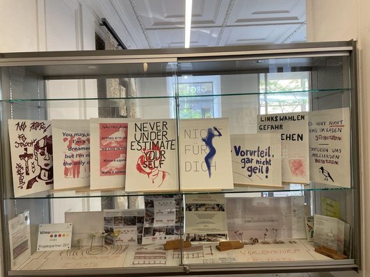 In einer Vitrine in der Schule sind selbstgefertigte Plakate sichtbar.