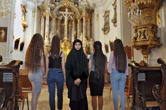 Foto in einer Kirche, vier Schülerinnen sind zum Altar gewendet, eine Schülerin mit Tschador blickt in die Kamera.