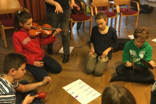 Foto von vier SchülerInnen, die mit Instrumenten rund um eine Notation am Boden sitzen