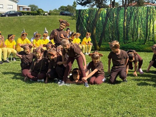 Kinder in Affenkostümen hocken in Wiese, Kinder in Löwenkostümen sitzen im Hintergrund