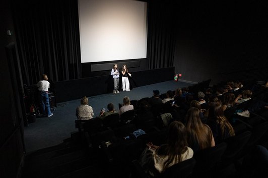 zwei Schülerinnen präsentieren vor Leinwand in dunklem Kinosaal