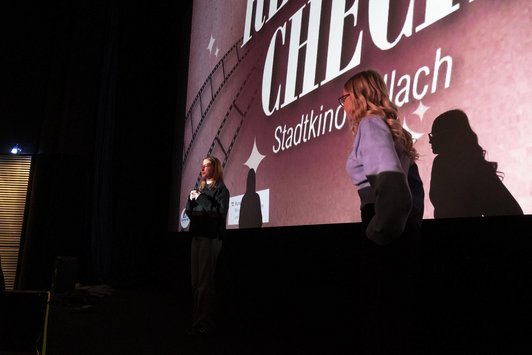 zwei Mödchen in dunklem Raum vor Projektsfläche, teilbeleuchtet von Projektion