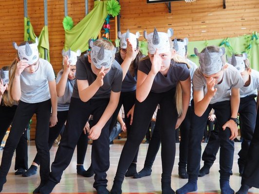 mehrere Kinder mit Nashorn-Masken vorgebeugt in identischer Pose
