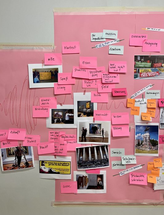 Foto einer Wand, die mit rosa Papier überzogen ist und auf der Fotos und beschriftete Post-Its hängen