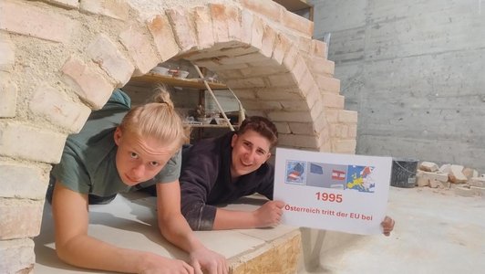 Foto von zwei Schülern unter einer selbstgemauerten Brücke mit einer Tafel 1995 Österreich tritt der EU bei.