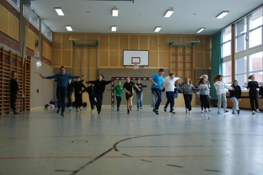 Schüler/innen einer Schulklasse bewegen sich im Turnsaal hüpfend nach vorne.
