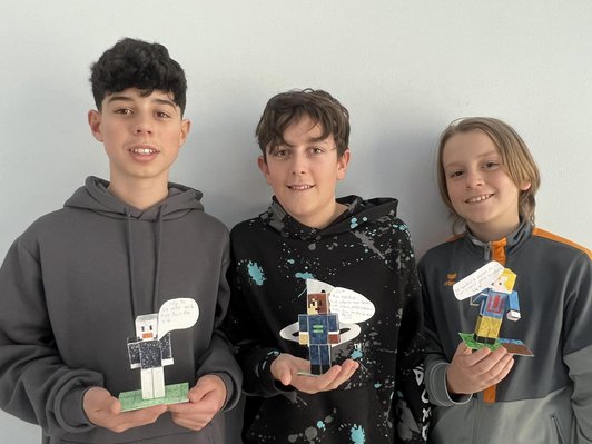 Drei Schüler mit gebastelten Minecraftfiguren aus Papier.