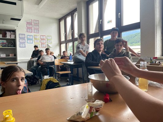 Hände über Schüssel auf Tisch, Schüler/innen im Hintergrund
