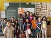 Dreizehn Kinder positionieren vor einer mit Kreide vollgeschriebenen Tafel
