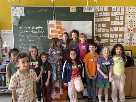 Dreizehn Kinder positionieren vor einer mit Kreide vollgeschriebenen Tafel