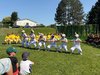 sechs Buben tanzen mit einer Kappe mit einem Horn auf dem Kopf in einer Wiese.