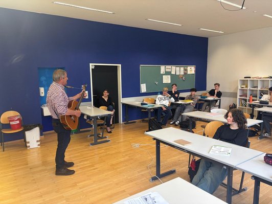 Musiker spielt auf einer Gitarre vor der Klasse
