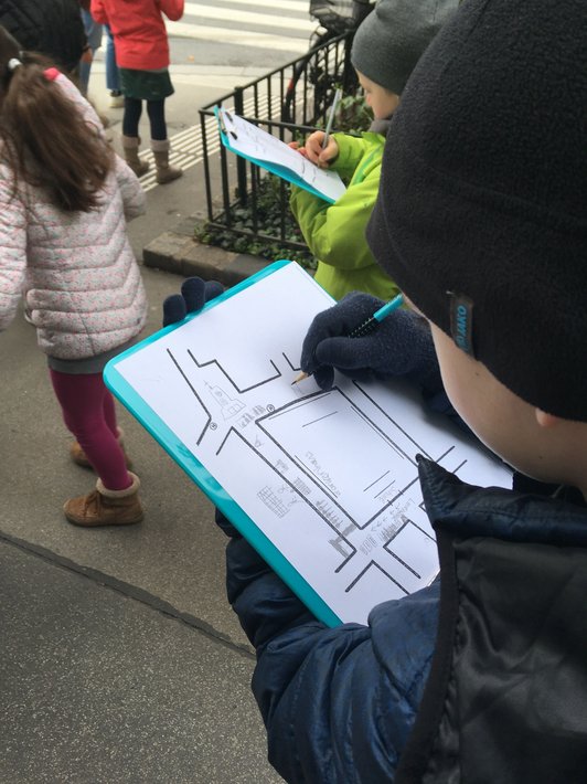 Foto von zwei Schülern auf Stadtexkursion, die im Freien mit einem Klemmboard, einem Plan und einem Bleistift arbeiten