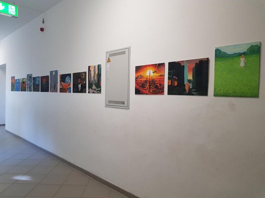 Ausstellungsansicht der entstandenen gemalten Werke im Informatikgang der Schule. Verschiedene bunte Bilder, z.b. Mädchen auf Blumenwiese, Stadtansichten etc.,