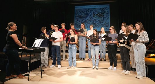 Schüler/innen stehen im Kreis und werden von einer Musikerin am Keyboard begleitet