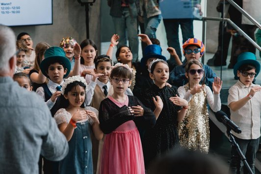 Gruppenbild mit Mädchen mit schönen Haarbändern und Burschen mit Hüten stehen bei einem Stiegenaufgang.
