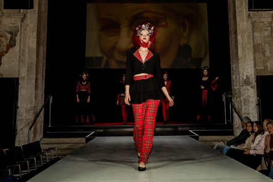 Foto der Fashionshow. Eine Schülerin im Vordergrund und 4 im Hintergrund. Alle tragen rotkariert/schwarz individuelle Kleidungsstücke.