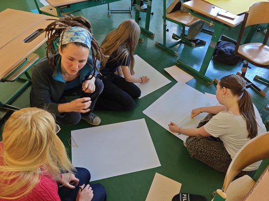 Foto von drei Schülerinnen sitzend am Boden zeichnend und der Workshopleiterin.