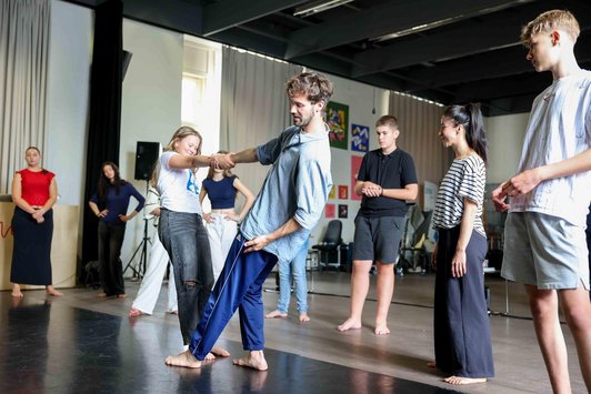 Tänzer stellt eine Tanzbewegung mit einer Schüler/in vor, andere schauen zu.