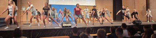 Eine Klasse tanzt auf einer Bühne eine Choreografie.