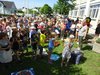 Foto von einer Erwachsenen mit Mikrofon und vielen klatschenden Schüler/innen bei der Präsentation von Betonhockern mit Mosaiken im Schulgarten