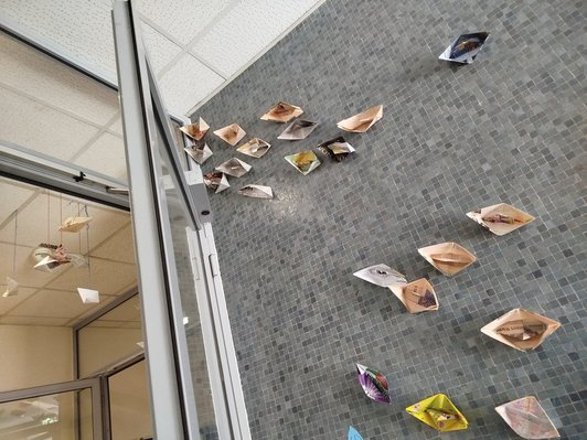 Foto einer grauen Fliesenmauer mit gebastelten Papierbooten
