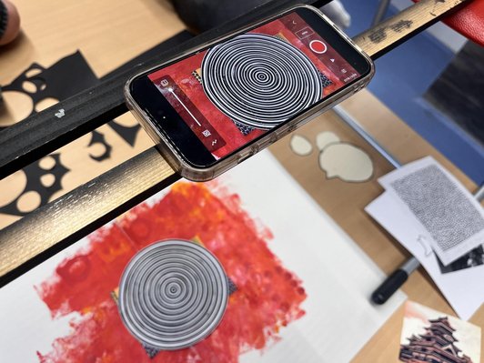 Handy liegt auf einer höher gelegenden Holzlatte, um mit Abstand einen dreidimensionalen Kreis auf einem Papier fotografieren zu können.