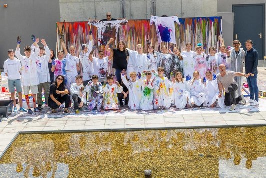 Schulklasse in bunt-befleckter Schutzkleidung und Erwachsene vor Schüttbild