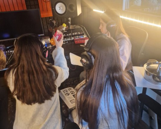 Foto von drei Schülerinnen mit Kopfhörern in einem Studio.