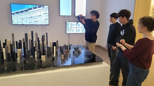 vier Jugendliche stehen neben Modell aus Steinquadern, einer fotografiert