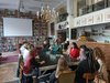 Zehn Schüler/innen und eine Referentin sitzen um einen Tisch in einer Bibliothek.