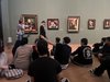 Schüler/innen sitzen am Boden in einem Kunstmuseum und diskutieren mit einer Kunstvermittlerin, die vor einem Bild steht.