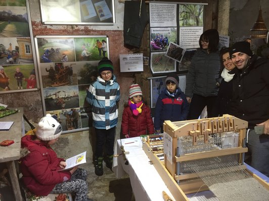 Foto von vier jungen und drei erwachsenen AusstellungsbesucherInnen rund um einen Webstuhl