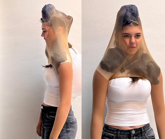 Schülerin mit über Arme und Kopf gezogener Strumpfhose und in diese und Shirt gestopften Textilien