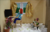 Videostill eines Animationsfilms mit gebastelter Person vor einem Scheibtisch mit Computer, einem Fenster mit gelben Brümchenvorhang, Pflanzen einer Diskokugel am Boden.