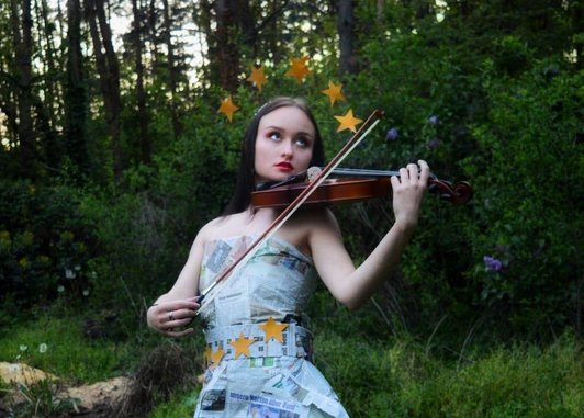 Foto einer Schülerin im Wald mit einer Geige. Sie trägt ein Kleid aus alten Zeitungen.