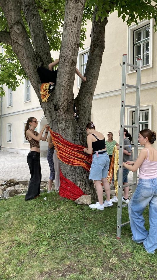 Schülerinnen umhüllen Baum mit Farbstreifen