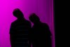 Zwei schwarze menschliche Silhoutten stehen vor lilla Hintergrund