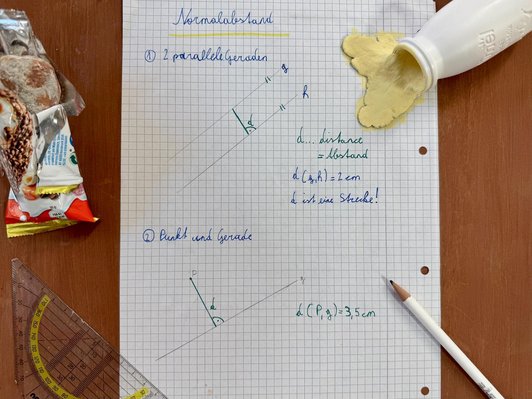 Foto von einem Karierten Zettel mit mathematischen Grafiken. Um den Zettel herum ein Geodreieck, ein Beistift, eine angebissene Süssigkeit und eine ausgeschüttete Plastikflasche mit gelber Flüssigkeit.